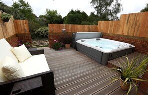 A hot tub on a wooden deck with a sofa and potted plants. - The Three Lions (Fordingbridge)