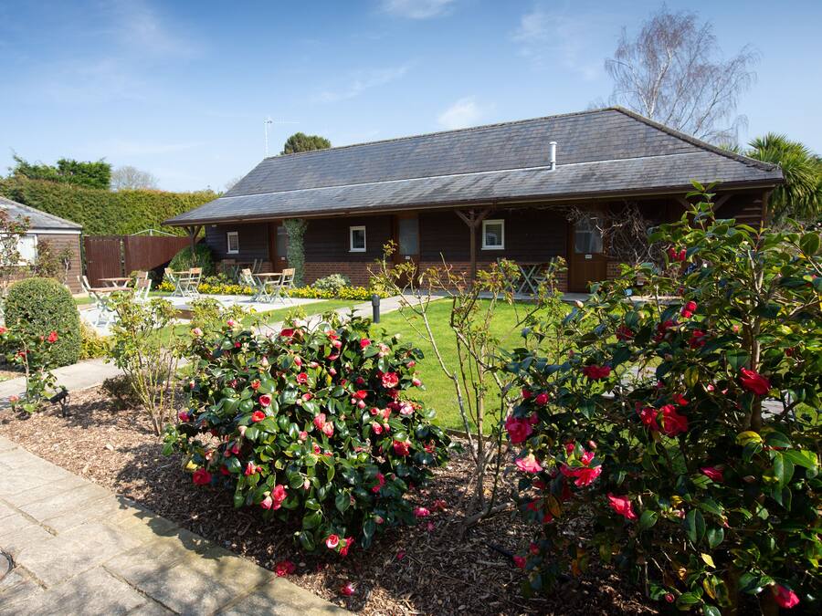 A house with a sloped roof, a front porch, and a well-maintained garden with flowering bushes.