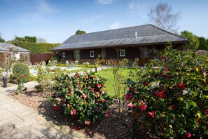A house with a sloped roof, a front porch, and a well-maintained garden with flowering bushes. - The Three Lions (Fordingbridge)