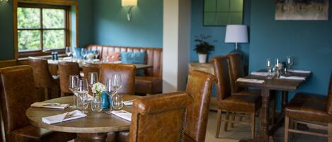 A dining area with wooden tables and chairs, a bench, and a wall-mounted lamp.