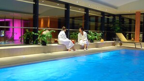 Un espace aménagé au bord de la piscine, avec deux personnes vêtues de robes blanches, une balustrade en verre et des plantes d’intérieur.