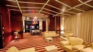 Un hall d’hôtel moderne avec un tapis à rayures, des fauteuils en cuir, un téléviseur et un coin bar.