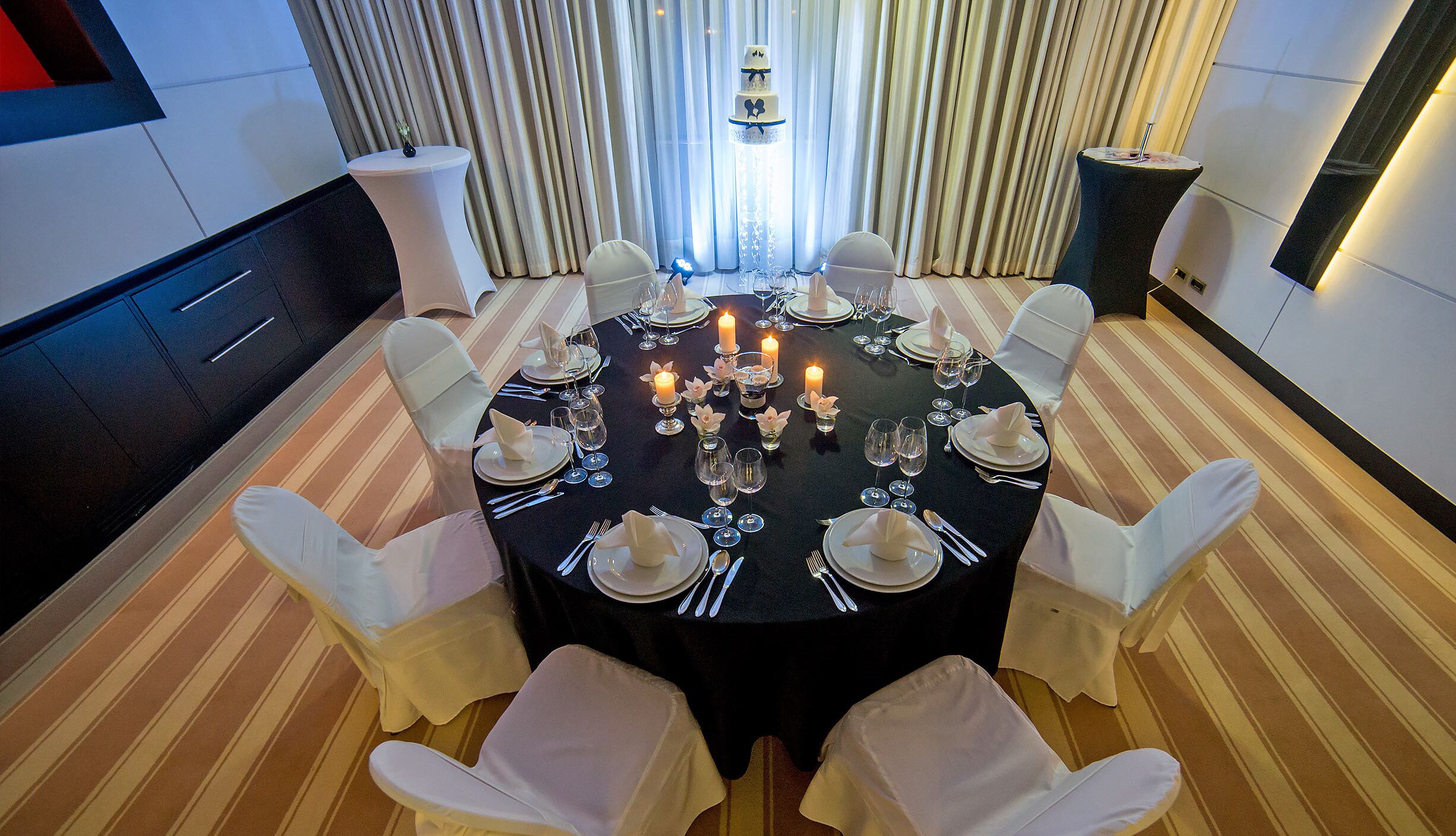 A round dining table set for six with white chairs, candles, and a tiered cake.