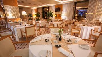 Un comedor bien iluminado y elegantemente dispuesto, con varias mesas preparadas para el servicio, con sábanas blancas, cubertería ordenada y cristalería.