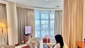Une chambre d’hôtel dotée d’une grande fenêtre, d’un téléviseur, d’un canapé, d’une table basse et d’une tablette.