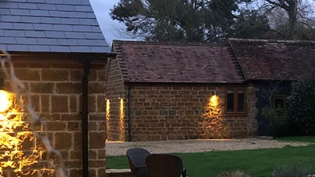 A stone building with a brick extension, outdoor seating, and a well-maintained lawn. - Wisteria Cottage - Cotswolds (Warmington)