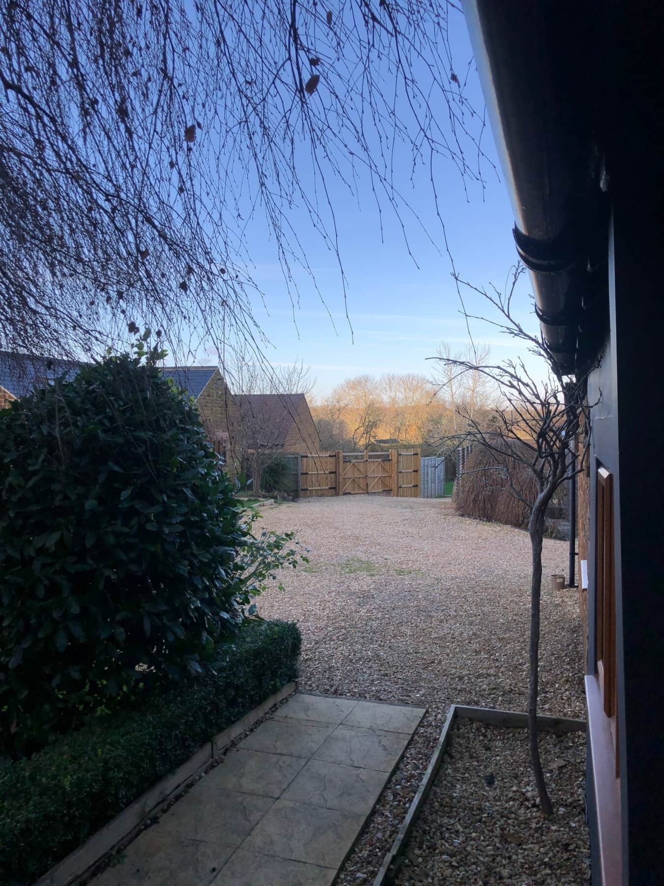Une allée de gravier mène à une maison entourée d’une clôture en bois et dotée d’un portail en métal.