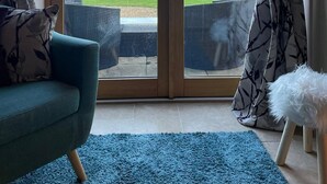 A room with a sliding glass door leading to an outdoor area with a wooden deck and chairs. - Wisteria Cottage - Cotswolds (Warmington)