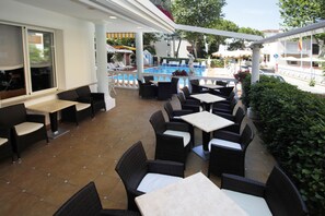 An outdoor patio area with wicker furniture and a pool. - Hotel Villa dei Fiori (Rimini)