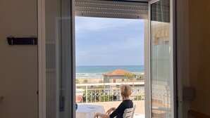 A room with a bed, a balcony with a view of the sea, and a person sitting on a chair. - Hotel Villa dei Fiori (Rimini)