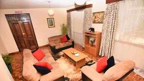 A living room with a sofa set, a coffee table, and a wooden cabinet. - GraceHouse Resort (Nairobi)