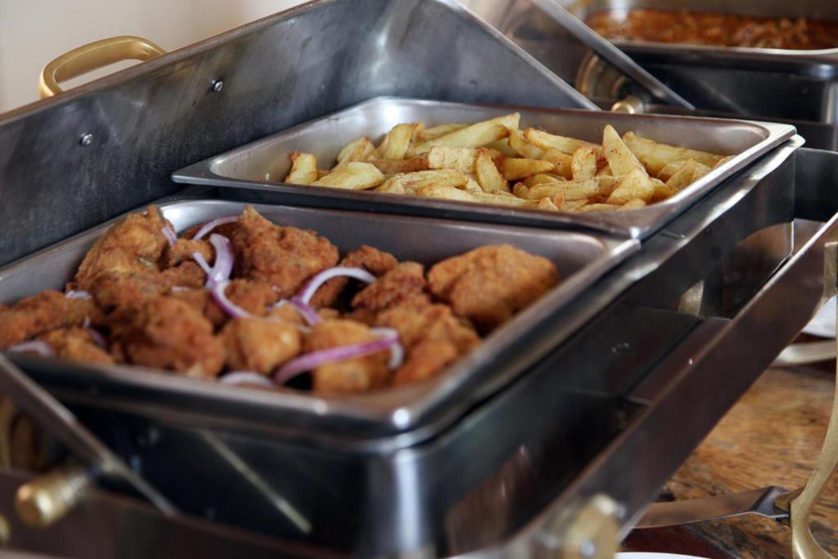 A buffet with trays of fried chicken and French fries.