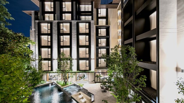 A modern building with multiple floors, large windows, and a pool area with seating. - Gardina Asoke Hotel & Residence (Bangkok)