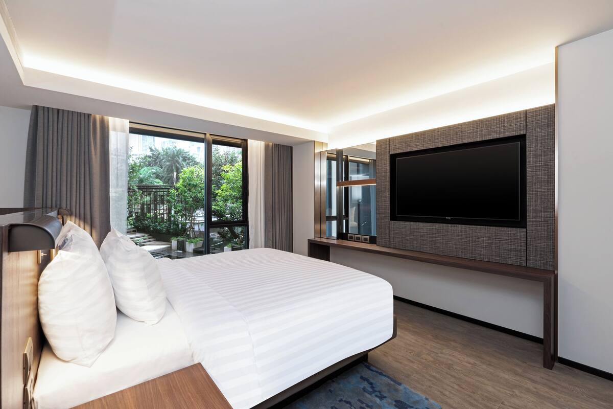 Habitación de hotel moderna con una cama grande, un televisor de pantalla plana en la pared y vistas a zonas verdes.