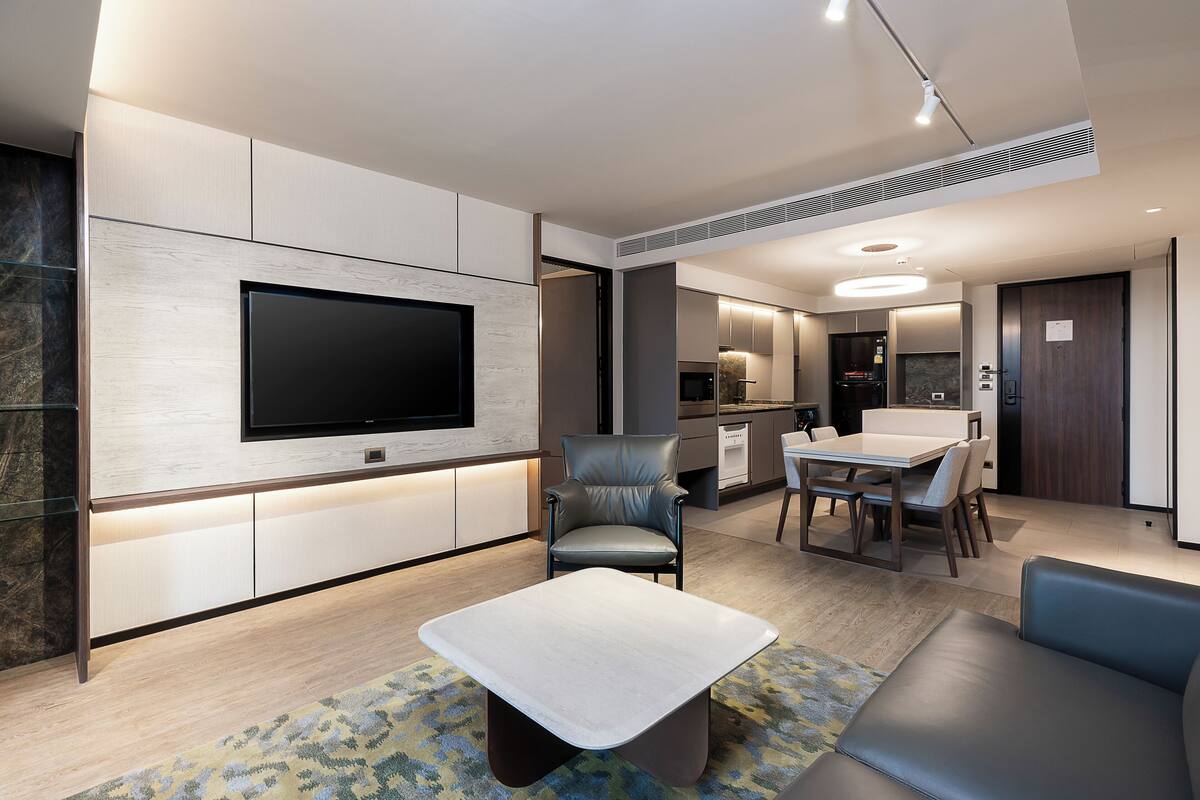 Una sala de estar moderna con un televisor de pantalla plana, sofá de cuero y un comedor con mesa y sillas.