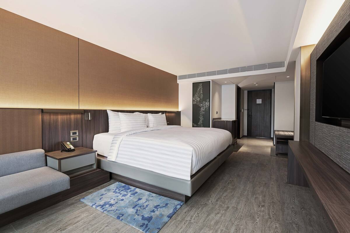 Habitación de hotel moderna con una cama grande, un sofá, un televisor de pantalla plana y un pequeño escritorio con teléfono.
