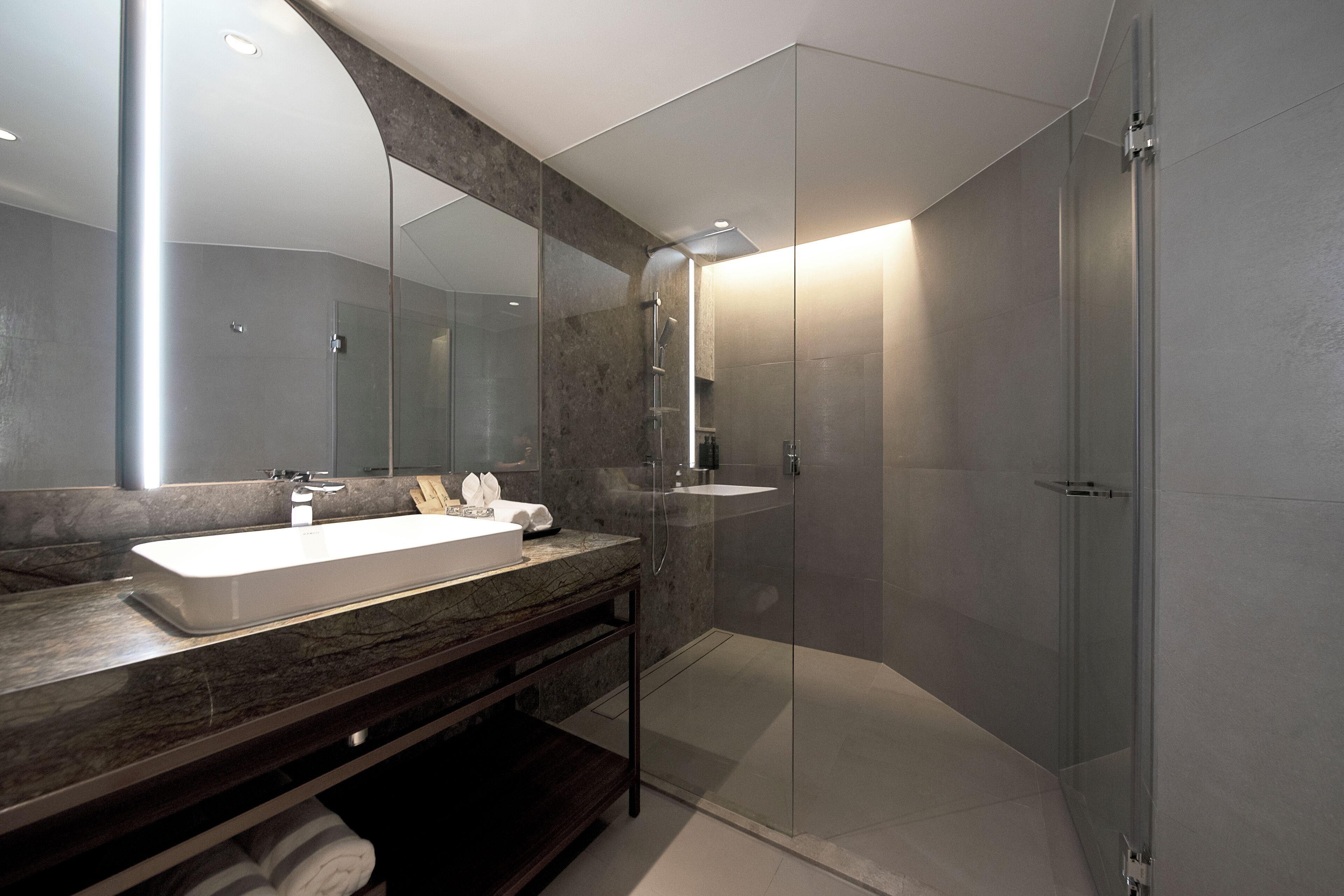 A modern bathroom with a large mirror, a white sink, and a glass-enclosed shower.