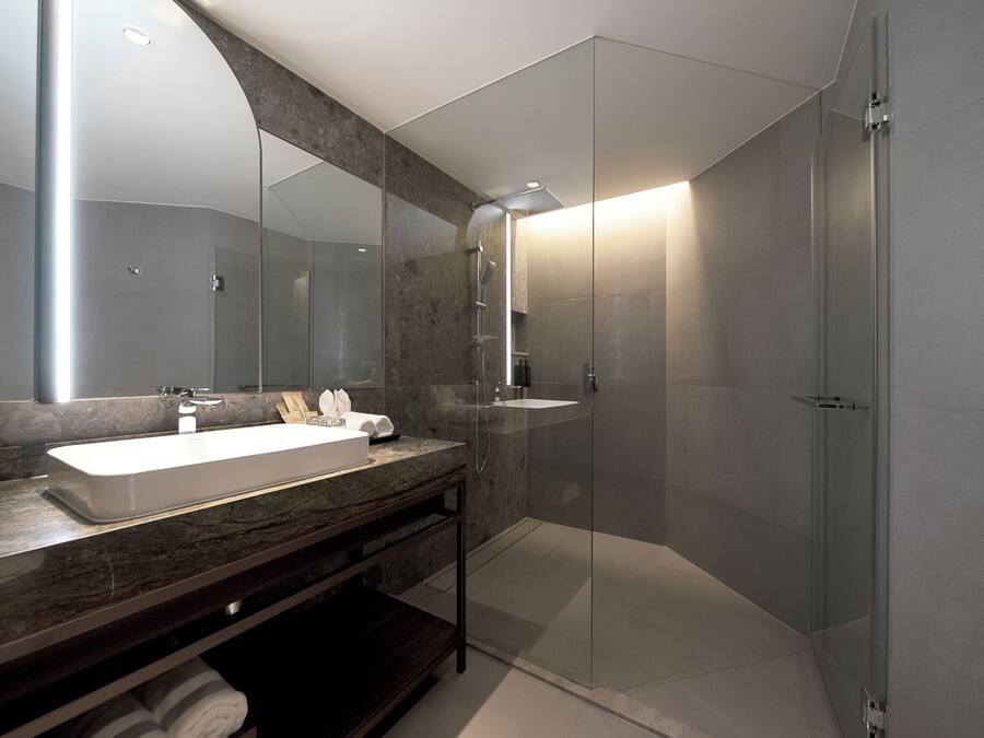 A modern bathroom with a large mirror, a white sink, and a glass-enclosed shower.