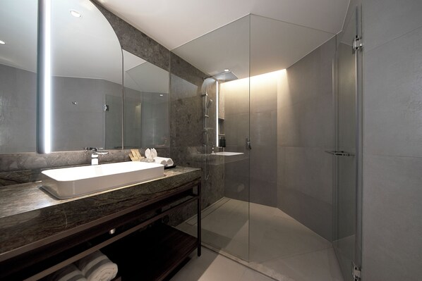 Une salle de bain moderne avec un grand miroir, un lavabo blanc et une douche à parois de verre.