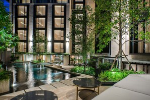 A modern building with a pool, outdoor seating, and greenery.