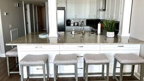 A modern kitchen with a granite island, stainless steel appliances, and bar stools. - Oceanfront! - All New! Ultra Modern Farmhouse Chic at the Beach! (Myrtle Beach)