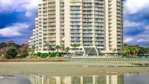 A high-rise hotel with multiple balconies, a reflective pool in the foreground, and a clear sky. - Oceanfront! - All New! Ultra Modern Farmhouse Chic at the Beach! (Myrtle Beach)