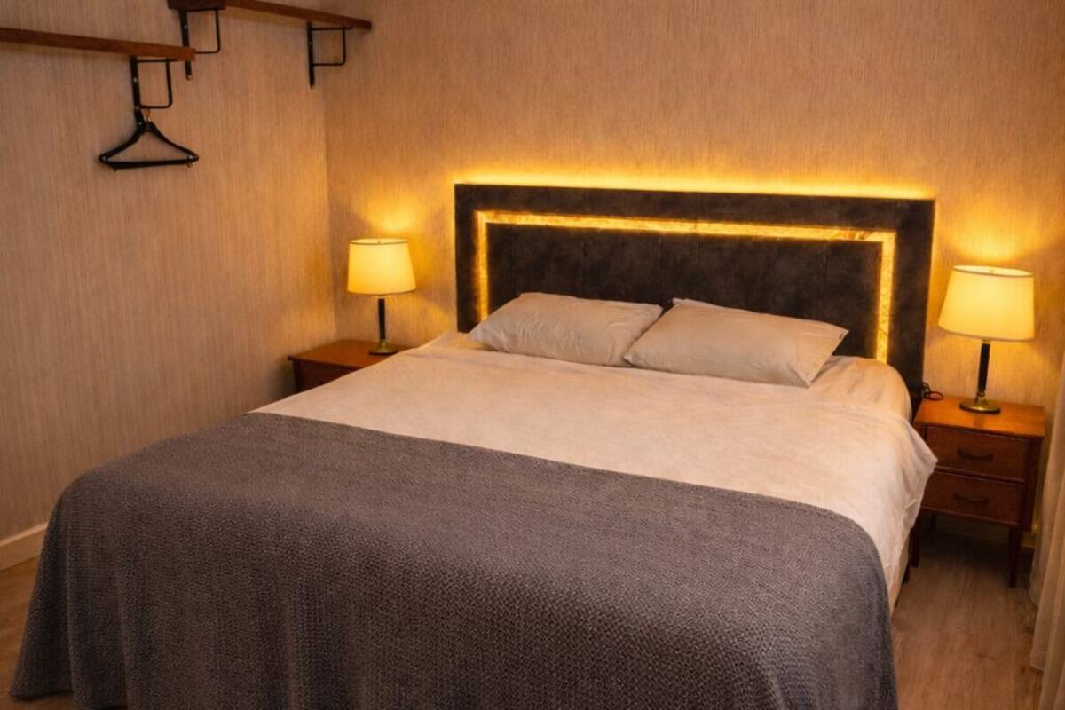 A neatly made bed with a dark grey bedspread, two bedside lamps, and a headboard with integrated lighting.