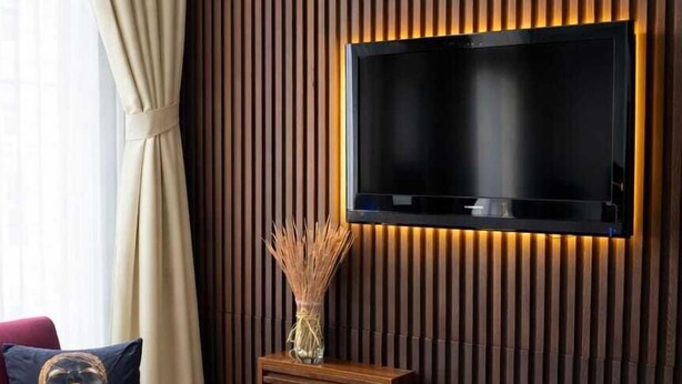 A modern living room with a flat-screen TV mounted on a wooden wall, a red sofa, and a glass coffee table. - Zebra Hotel Alsancak (Izmir)