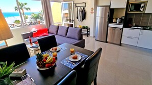 Une chambre d’hôtel moderne dotée d’un coin repas, d’une kitchenette et d’un balcon offrant une vue sur l’océan.