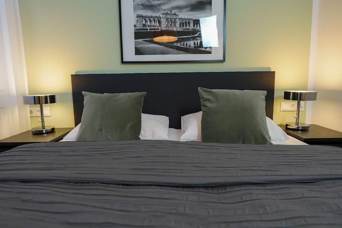 A hotel room with a large bed, two pillows, a framed picture on the wall, and two bedside lamps.