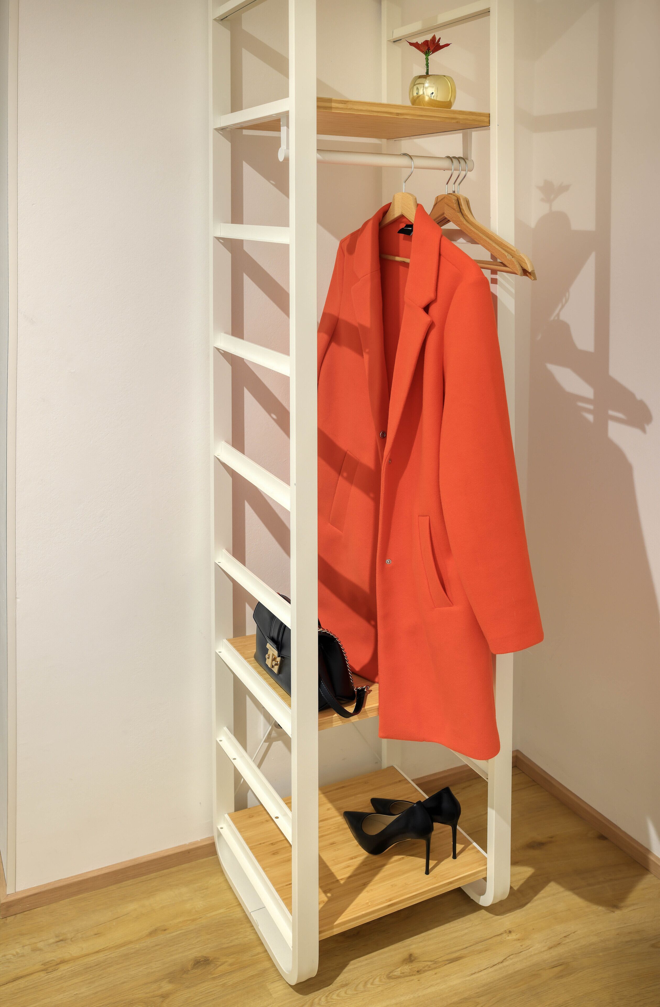 A white shelving unit with a red coat and black high heels.