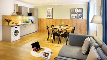 A modern kitchen with a built-in washing machine, dining area with wooden chairs, and a grey sofa.
