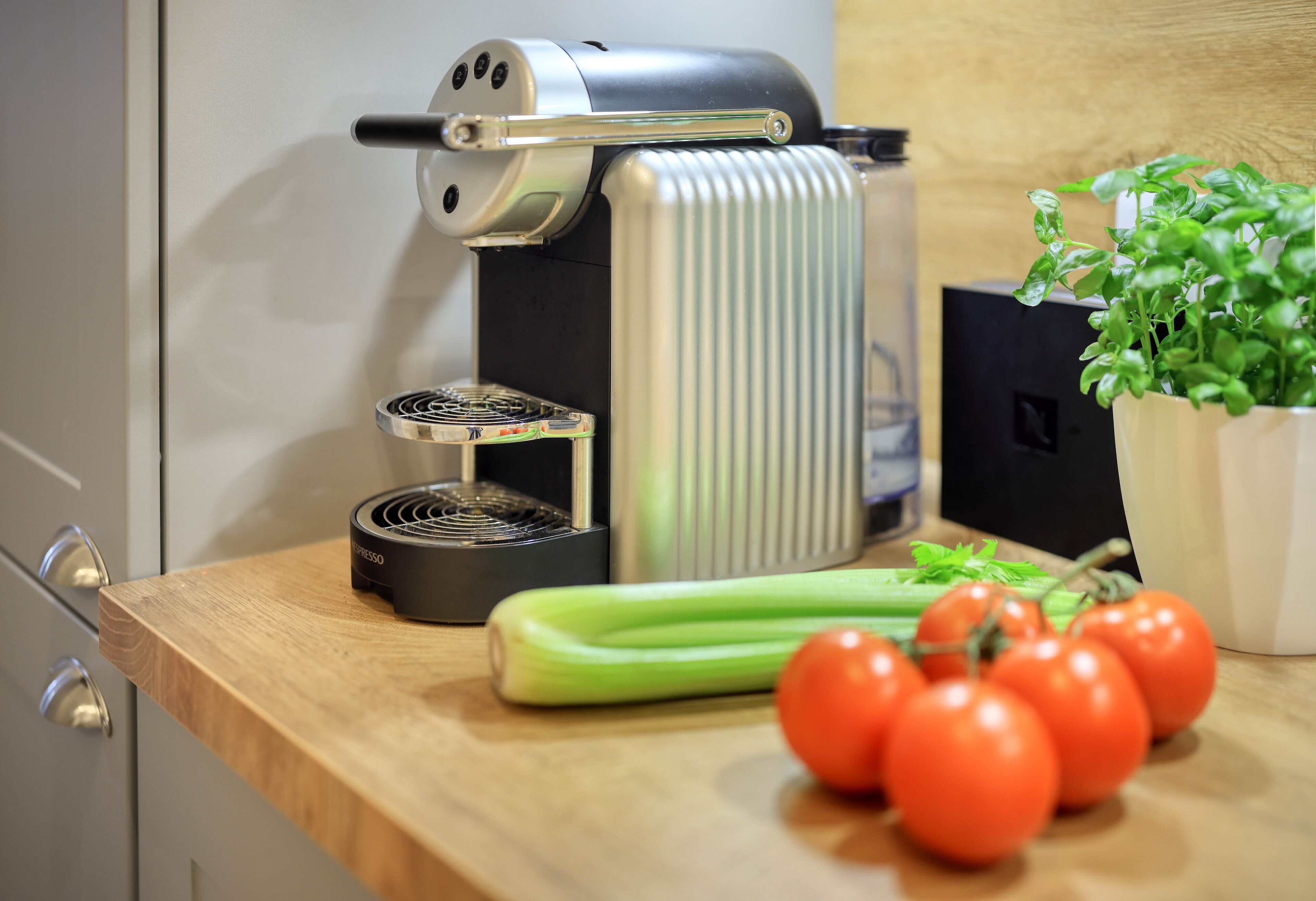 A kitchen with a coffee maker, a kettle, and fresh vegetables on the counter.