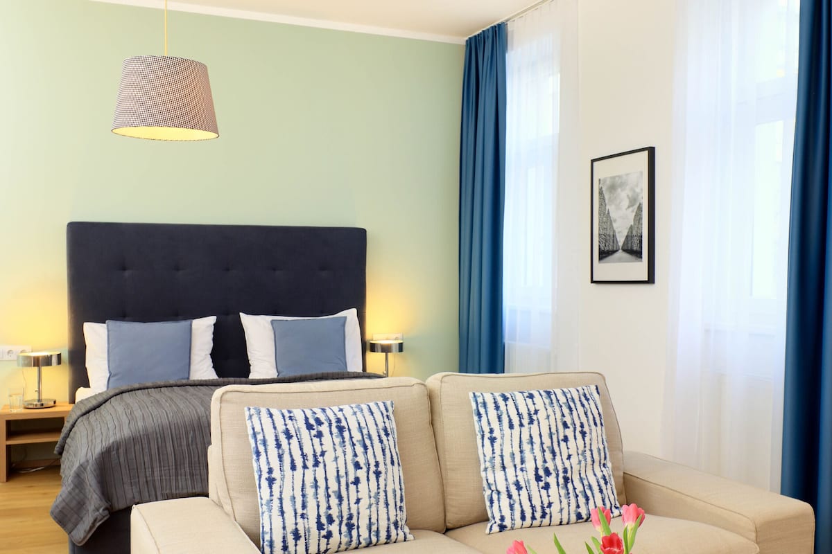 A modern hotel room with a bed, a sofa, a round coffee table, and a pendant light.