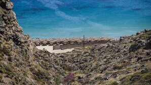 A rocky coastal landscape with a beach area featuring umbrellas and a wooden fence.