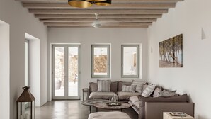 A modern living room with a sofa, a coffee table, and a lantern. There are large windows and a painting on the wall.
