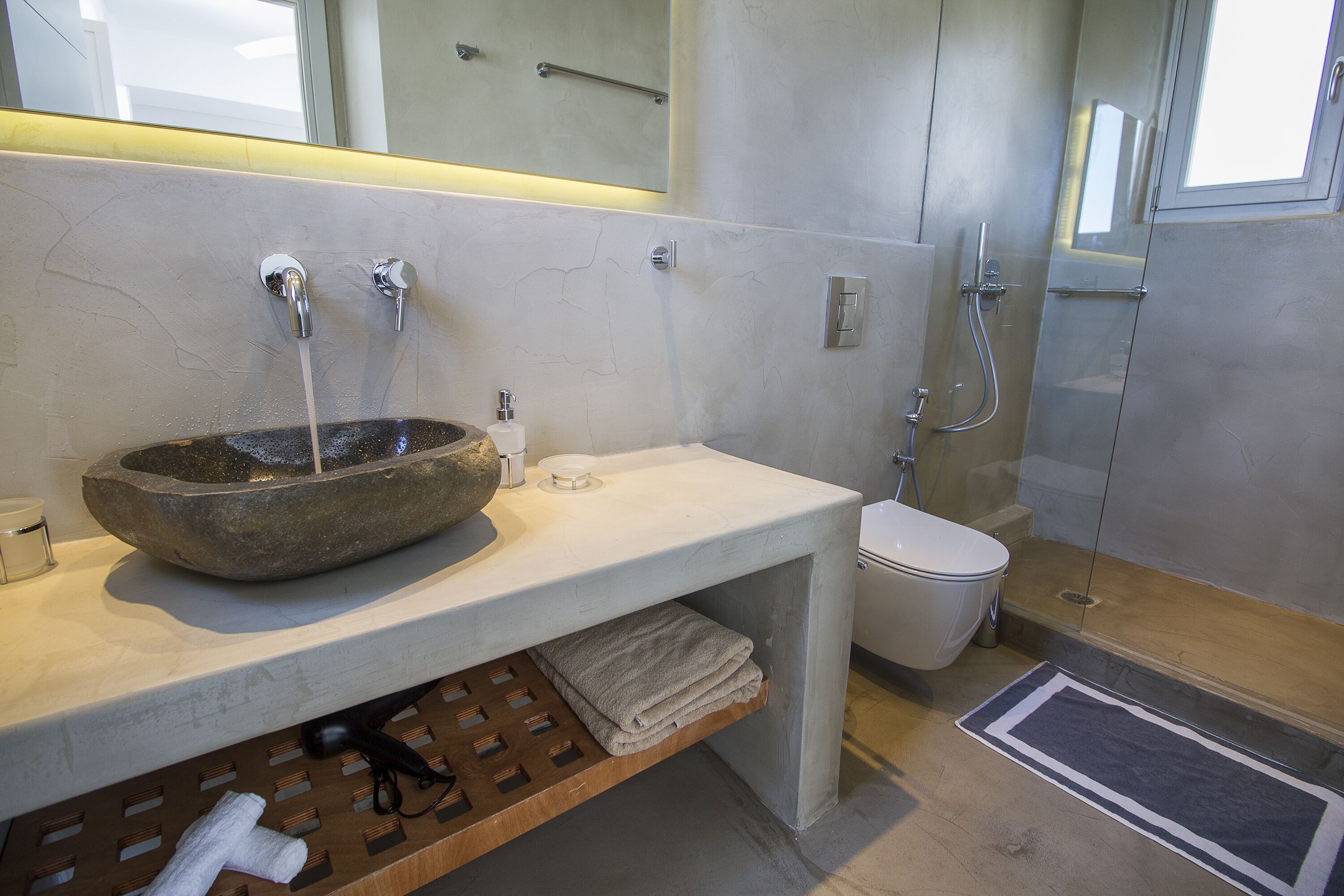 A modern bathroom with a stone basin, a toilet, and a shower.