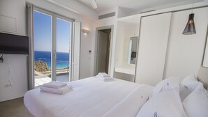 A hotel room with a bed, a TV, and a view of the ocean through a sliding door.