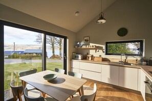 Une cuisine moderne dotée d’une grande fenêtre, un coin repas avec une table et des chaises, et une vue sur l’extérieur.