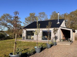 Une maison moderne en bois, dotée de grandes fenêtres, d’un porche couvert et d’une allée en gravier.