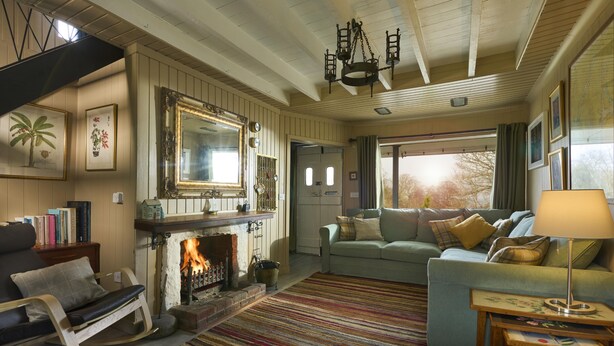 A cozy living room with a fireplace, a sofa, a rocking chair, and a large window with a view of trees. - The Moorings, overlooking Loch Fyne - sleeps 4 guests  in 2 bedrooms (Cairndow)