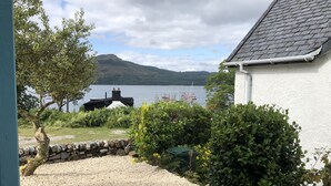 A house with a gravel driveway, a stone wall, and a view of a lake with a sailboat. - The Moorings, overlooking Loch Fyne - sleeps 4 guests  in 2 bedrooms (Cairndow)
