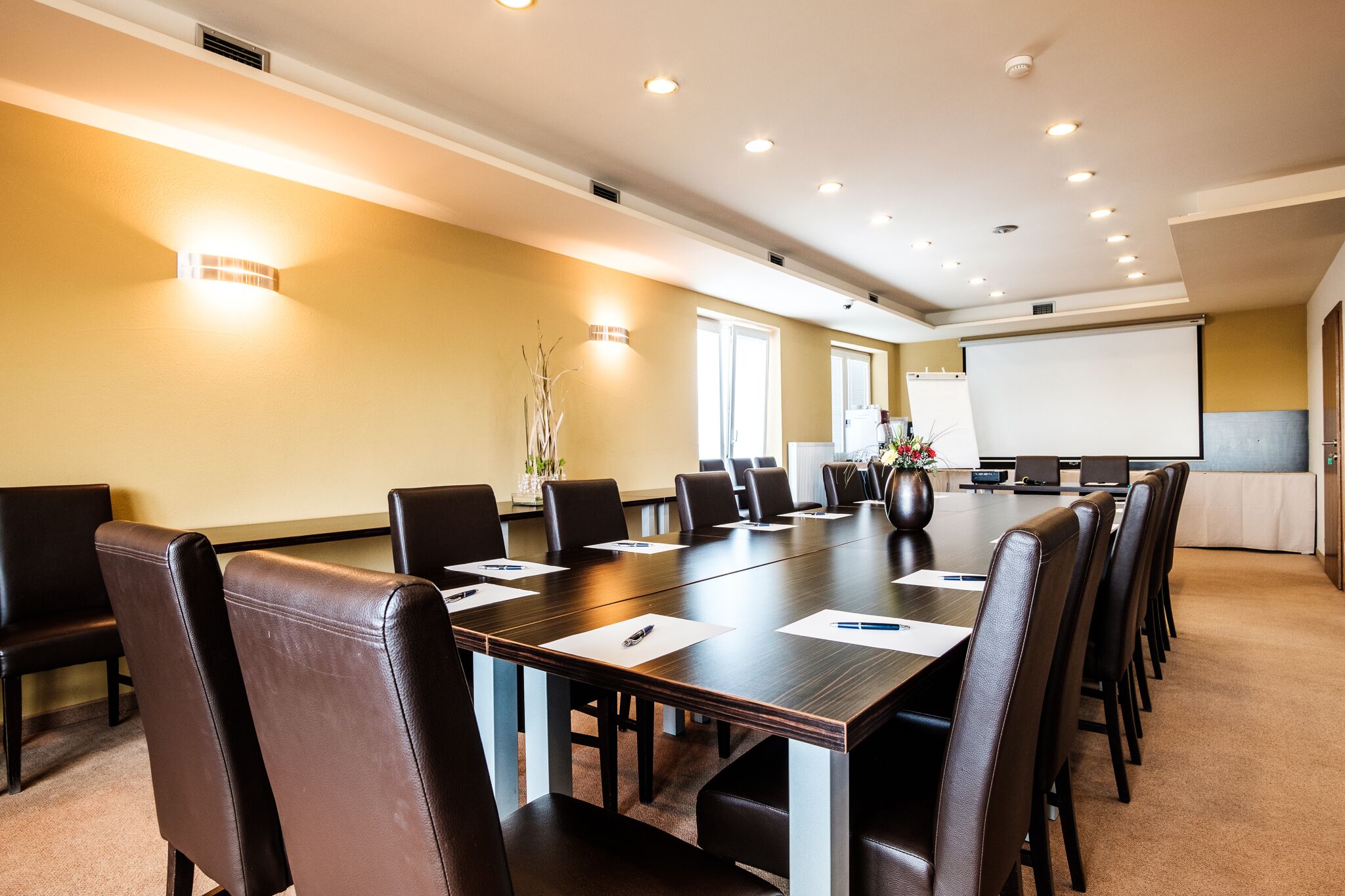 A conference room with a long table, chairs, a projector screen, and a whiteboard.