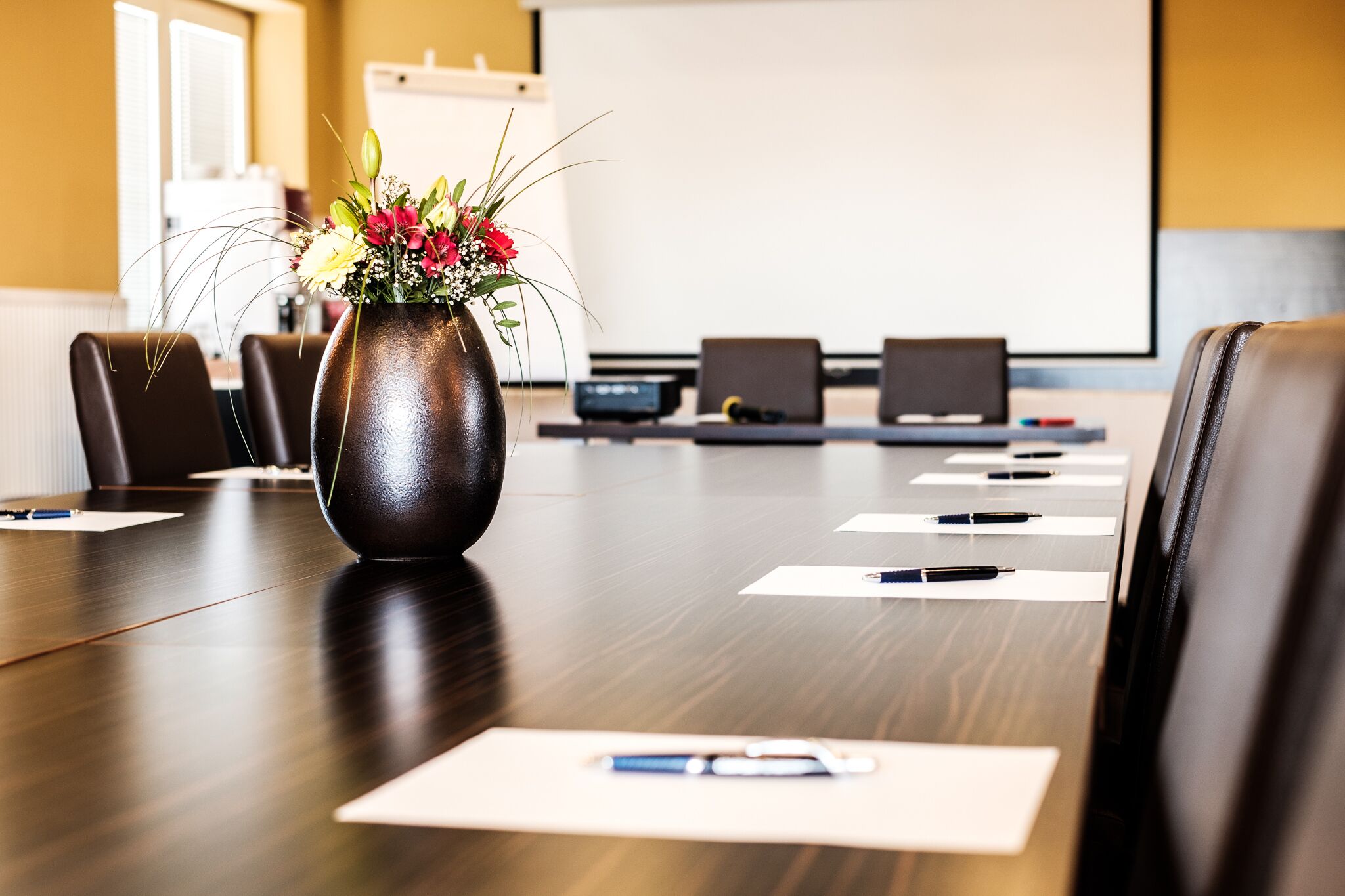 A conference room with a wooden table, a vase with flowers, and laptops.