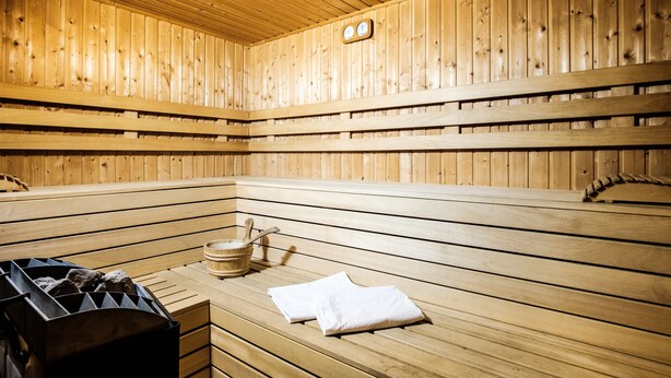 Una sauna de madera con bancos, un cubo de madera y un calentador de sauna.
