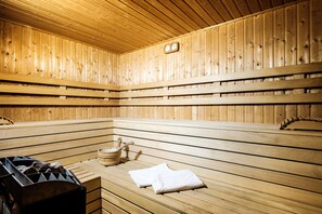Una sauna de madera con bancos, un cubo de madera y un calentador de sauna.