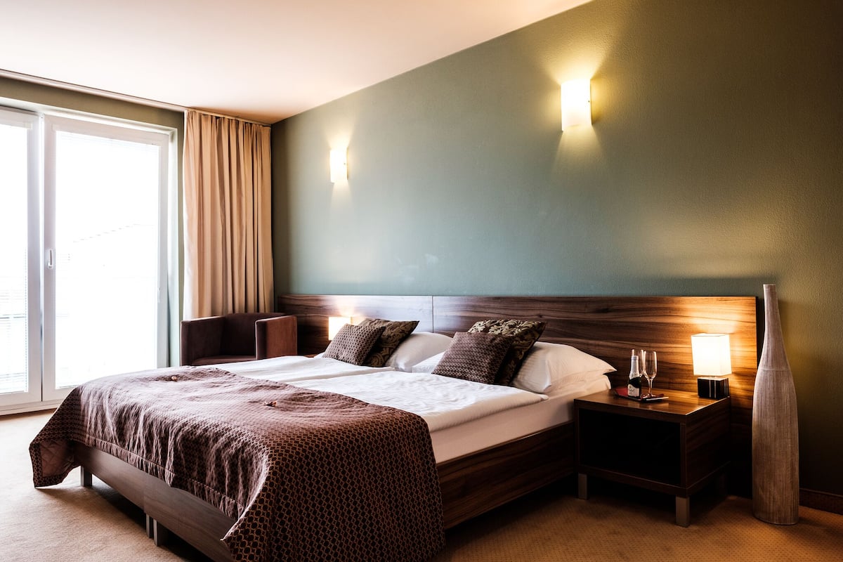 A hotel room with a large bed, a nightstand with a lamp, and a vase.