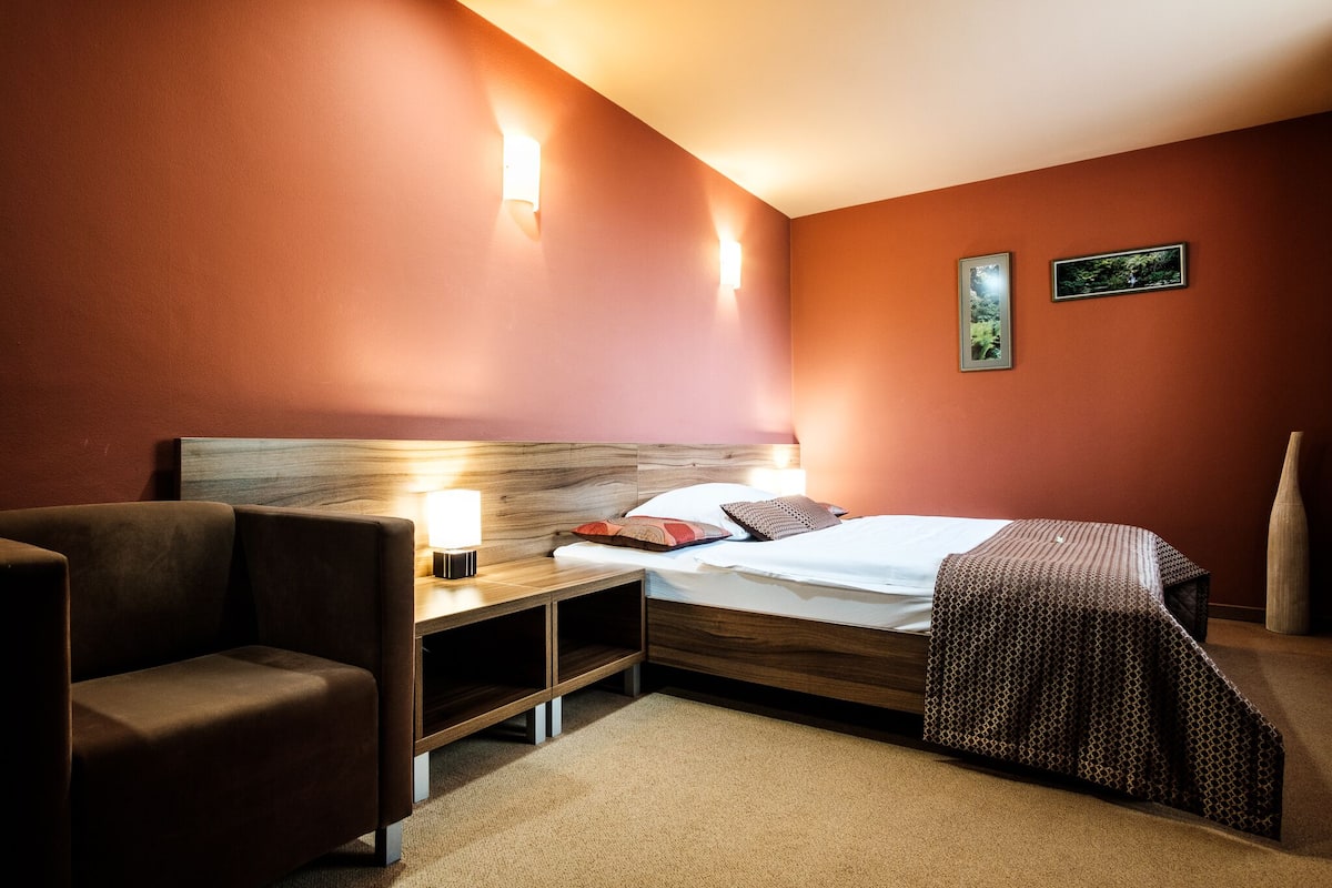 A hotel room with a bed, a nightstand with a lamp, a chair, and two wall-mounted lights.
