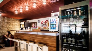 Zona de bar con mostrador de madera, taburetes y un refrigerador lleno de botellas.