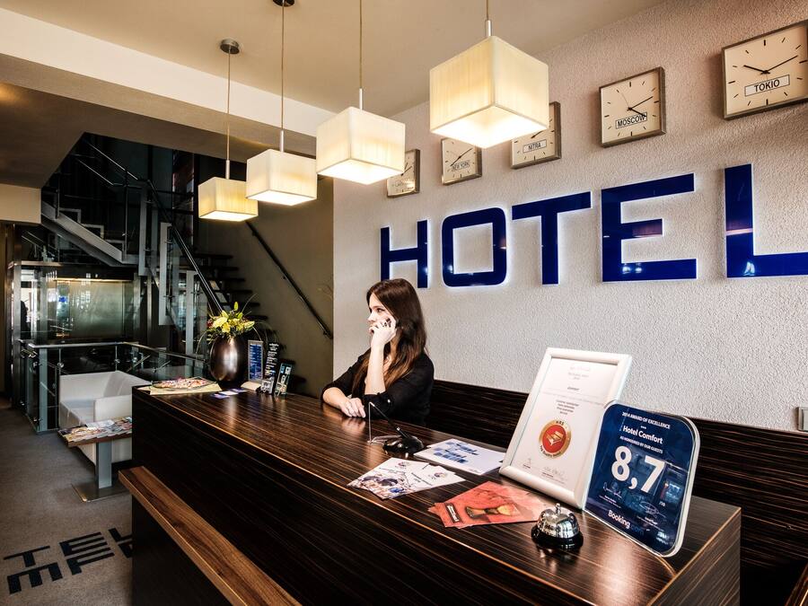 Hotellin vastaanottotiski, jonka yläpuolella on suuri kyltti, jossa lukee ”HOTEL”, sekä kello ja kyltti, jossa kerrotaan hotellin saaman arvosanan: ”Hotel Comfort”.
